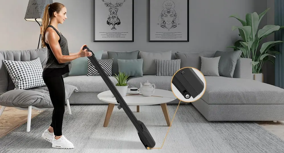 Compact walking pad on a living-room floor beside a sofa (retailer lifestyle image)