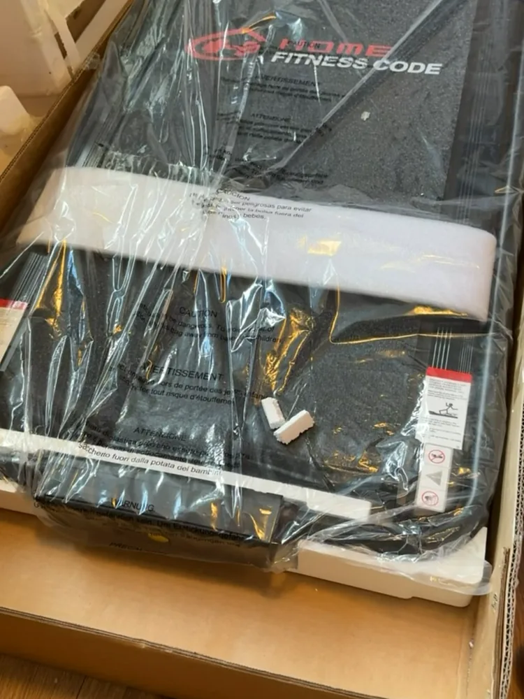 Home Fitness Code walking pad in its delivery box, wrapped in plastic film with white foam blocks at each end