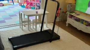 Black walking pad with a fold-up handrail set up on a cream rug in a family living room
